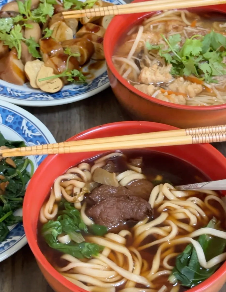 吃ㄐㄧˊ品素食的紅燒麵與羹麵,紅色湯碗裡有麵條、青菜與素料,旁邊配一盤素滷味與青菜