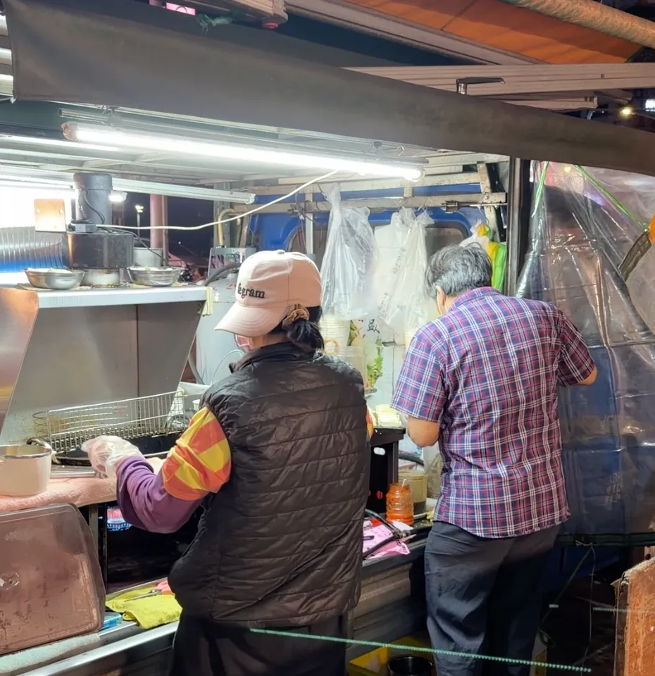 發財車臭豆腐的老闆與老闆娘在攤車前忙碌，老闆娘正用油鍋炸臭豆腐