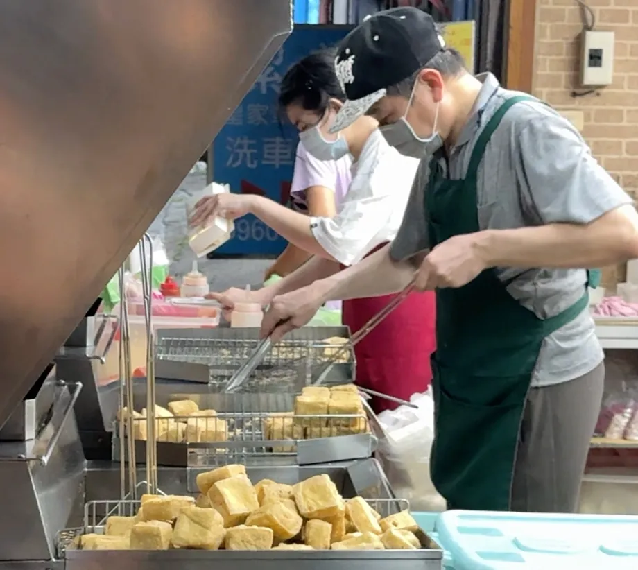 夜市港式脆皮臭豆腐現點現炸,老闆用長夾在油鍋前翻動整籃臭豆腐