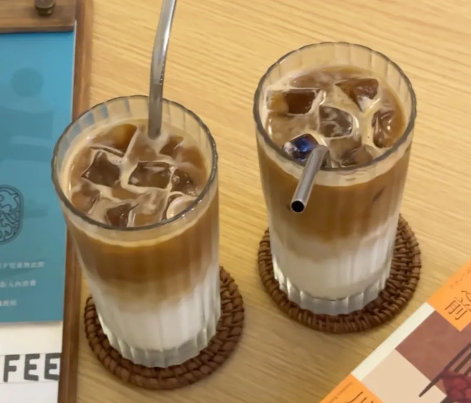 Q咖啡的兩杯冰拿鐵,牛奶與咖啡分層分明,裝在直紋玻璃杯裡放在藤編杯墊上