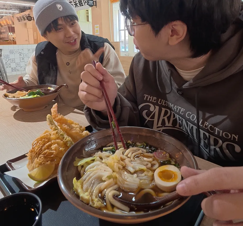在盛匠和食吃烏龍麵，碗裡有 Q 彈烏龍麵、溏心蛋、魚板與高麗菜，旁邊擺著天婦羅